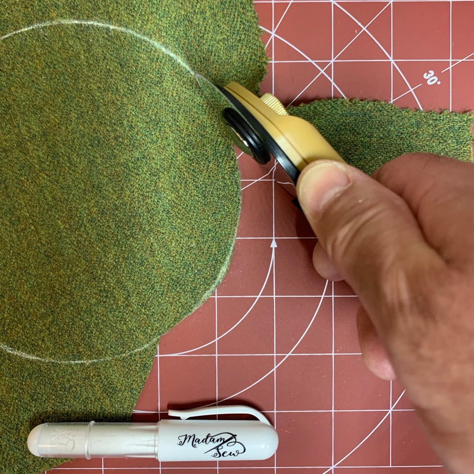 rotary cutter cutting on a curved chalk mark on a green fabric