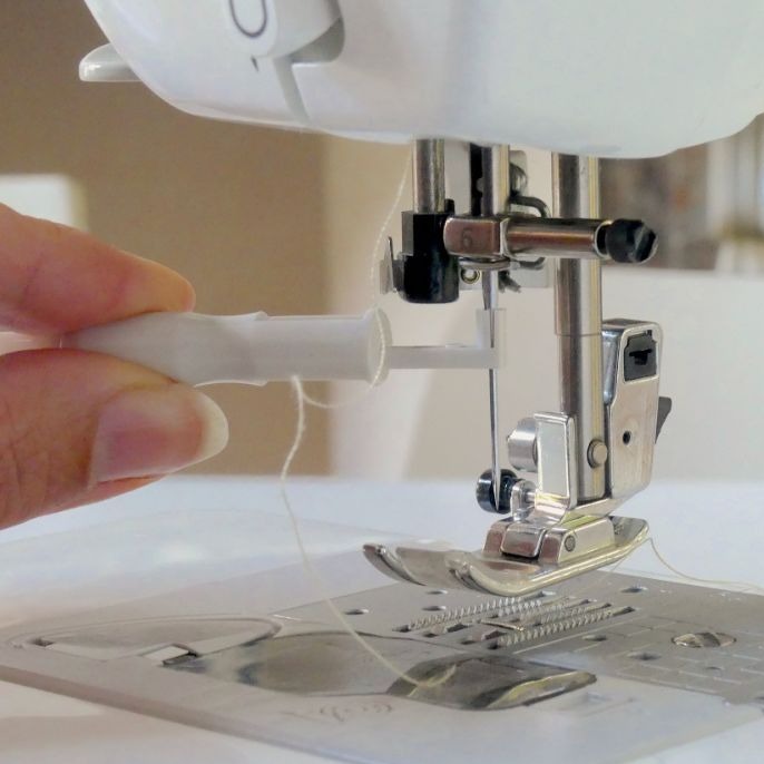 a hand is holding the needle inserter tool and is installing a sewing machine needle